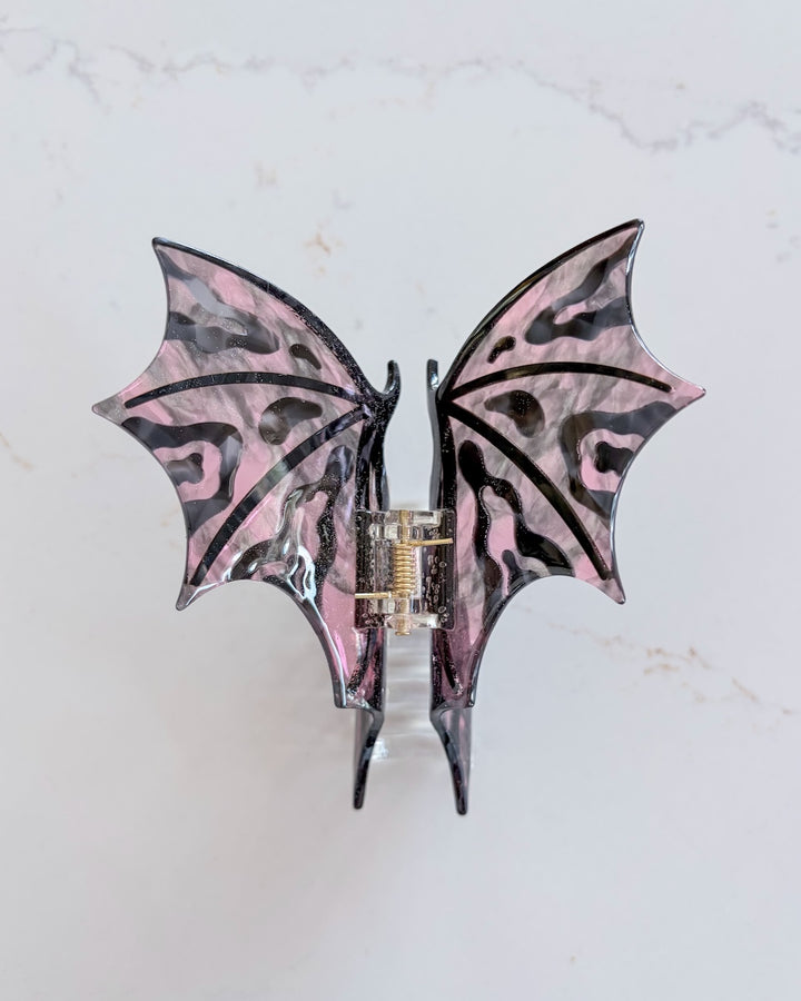 Pink and black dragon wing claw clip on a white marble background.