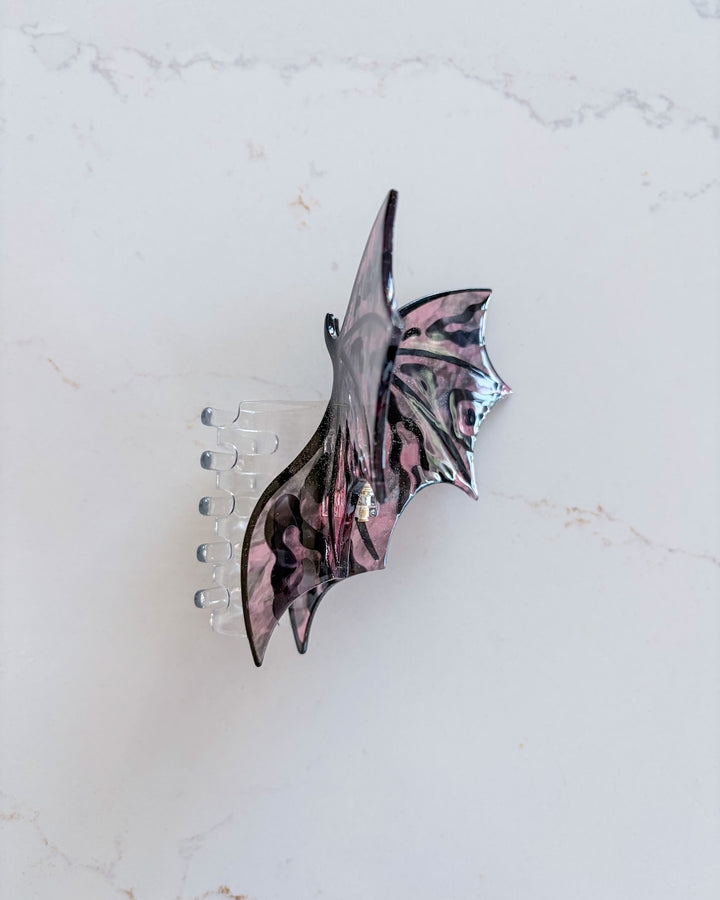 Side view of the dragon wing claw clips featuring a wing spread wide in pink and black all on a white marble background.