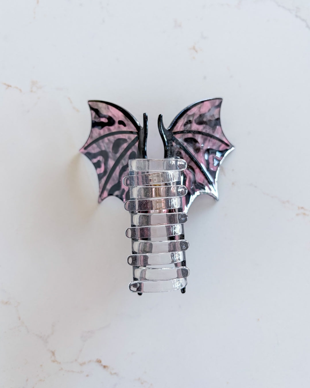 Hot pink and black dragon wing clip featuring the clear claw and the wings spread wide on a white marble background for fantasy fans.