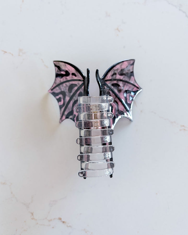 Hot pink and black dragon wing clip featuring the clear claw and the wings spread wide on a white marble background for fantasy fans.