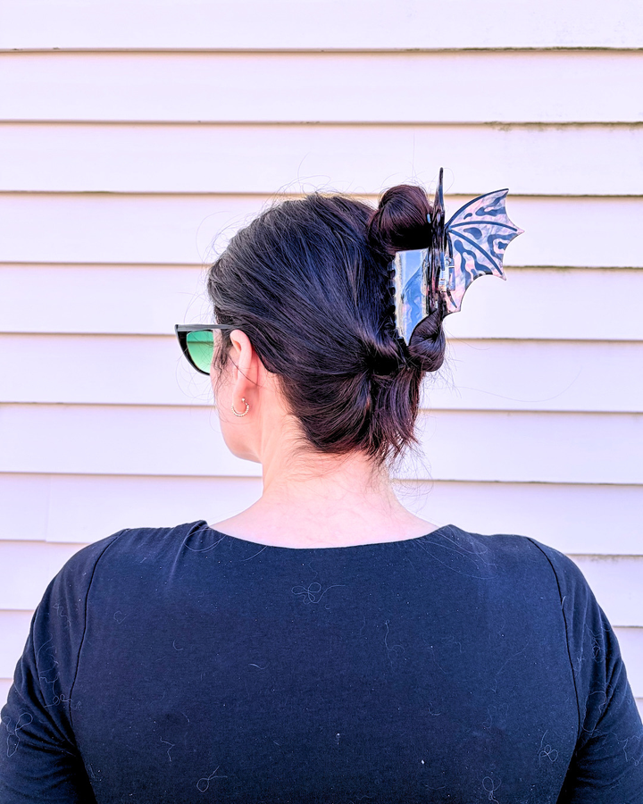 Woman with her head turned to the side, showing off a hot pink and black dragon wing hair clip for fantasy fans on a pinkish background.