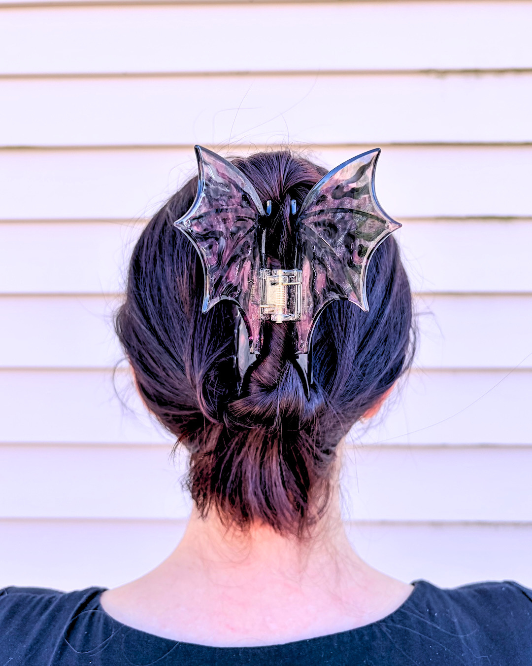 Woman wearing a dragon wing claw clip for fantasy lovers, featuring hot pink and black dragon wings spread wide on a pinkish background.