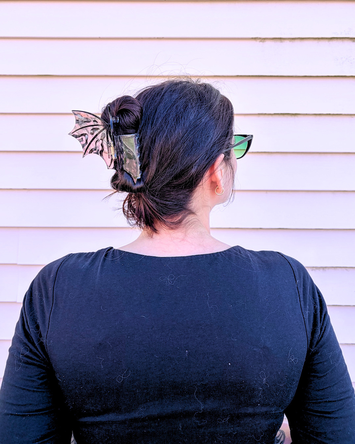 Woman wearing a dragon wing claw clip for fantasy lovers, featuring hot pink and black dragon wings spread wide on a pinkish background.