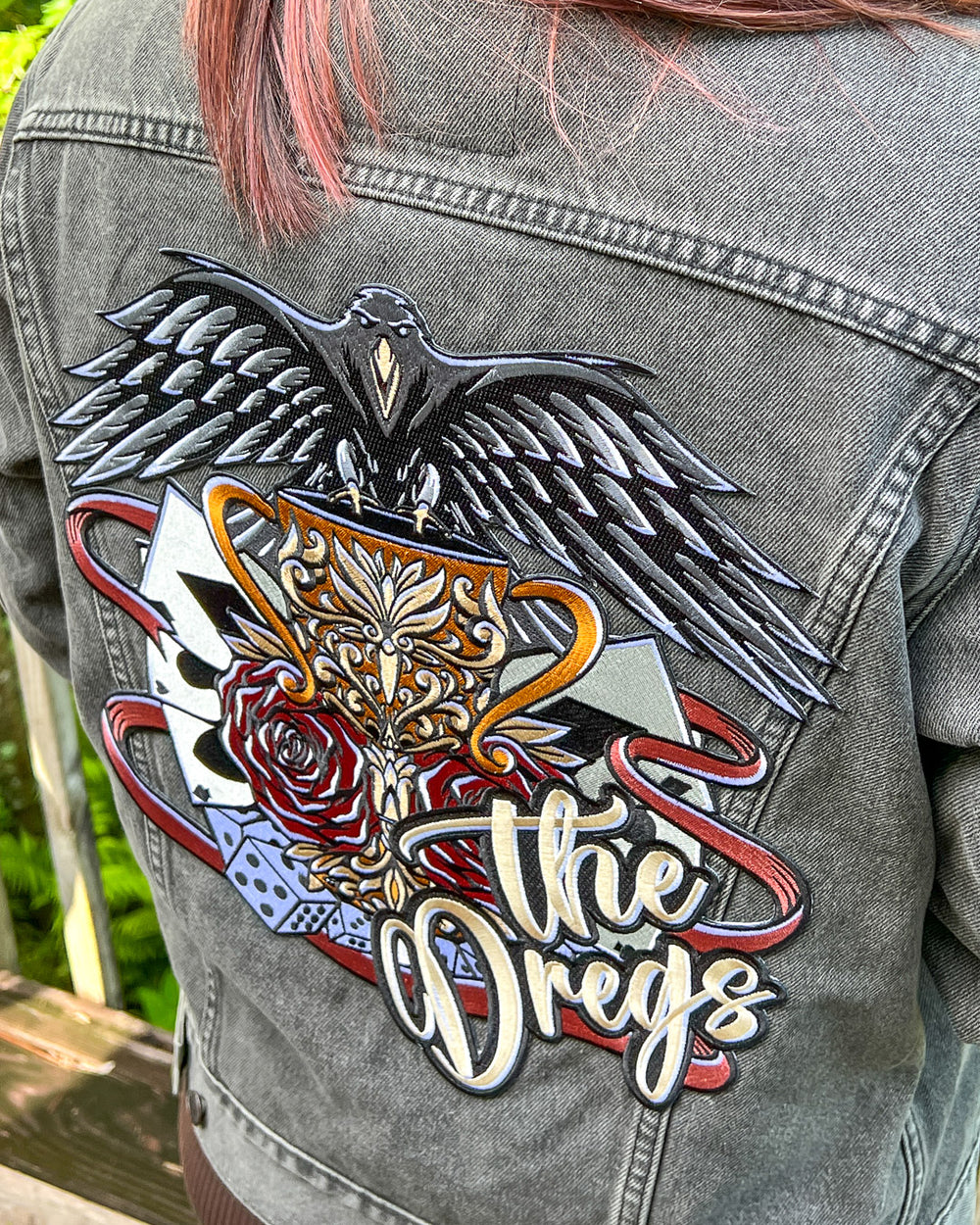 Iron-on patch for Six of Crows fans featuring a design with classic hallmarks of the crows including a crow, dice, and playing cards with 'the Dregs' written in the corner.