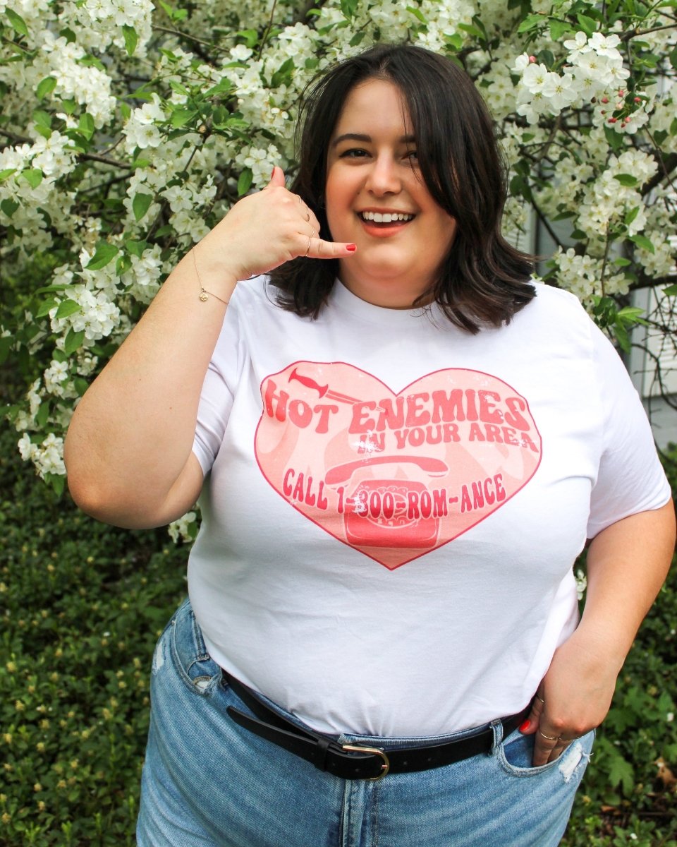 Romance shirt for enemies to lovers fans with 'hot enemies in your area, call 1-800-ROM-ANCE' written inside a heart with a phone, a dagger, and a phone.