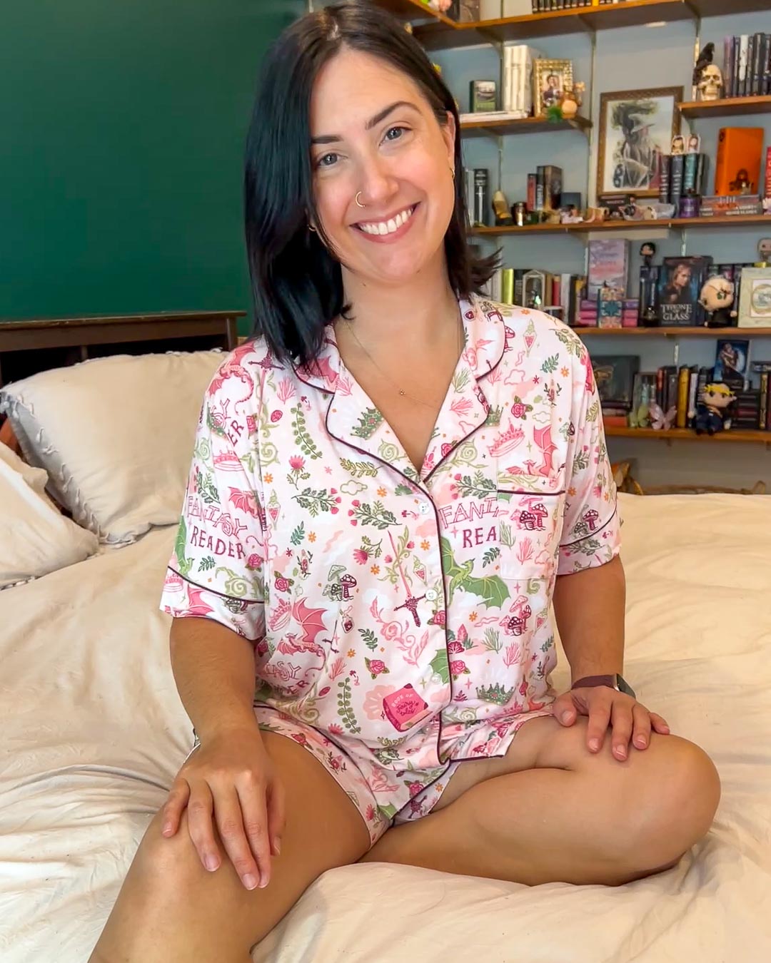 Model wearing the fantasy pajamas set featuring a collared shirt and stretchy shorts designed with illustrated swords, books, mushrooms, crowns, dragons, and more.