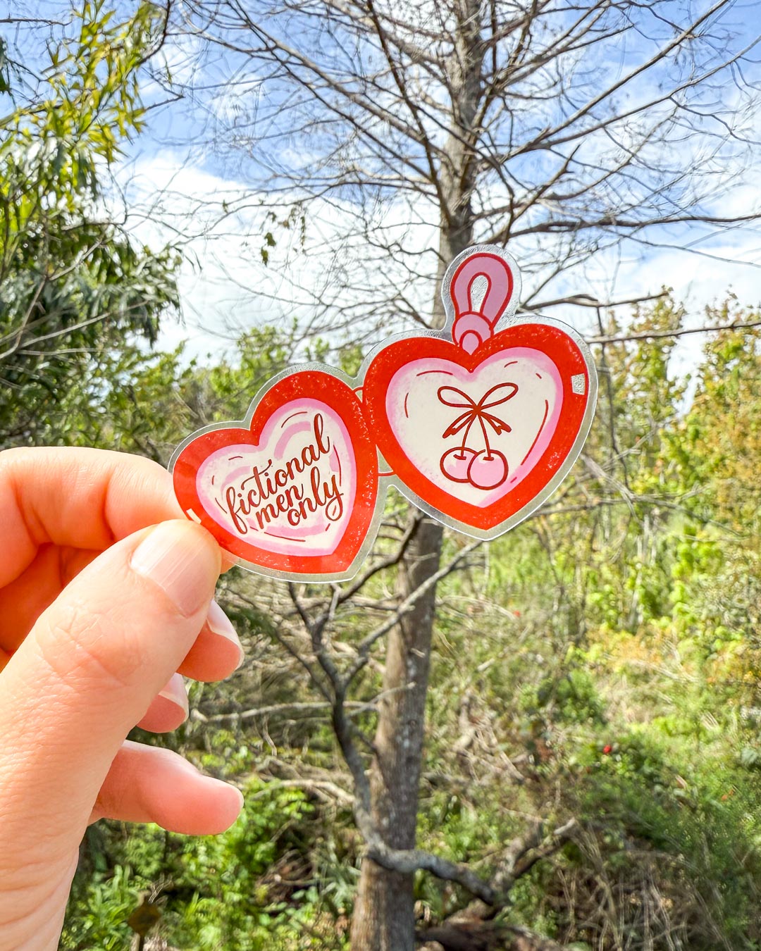 Red and pink sticker for book lovers featuring an illustrated design of a heart-shaped locket with two cherries on side and &