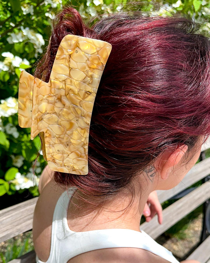 Hair clipped half-up-half-down with a gold pearlescent detailed bookish hair clip for fantasy readers designed to look like dragon scales with gem embellishments.