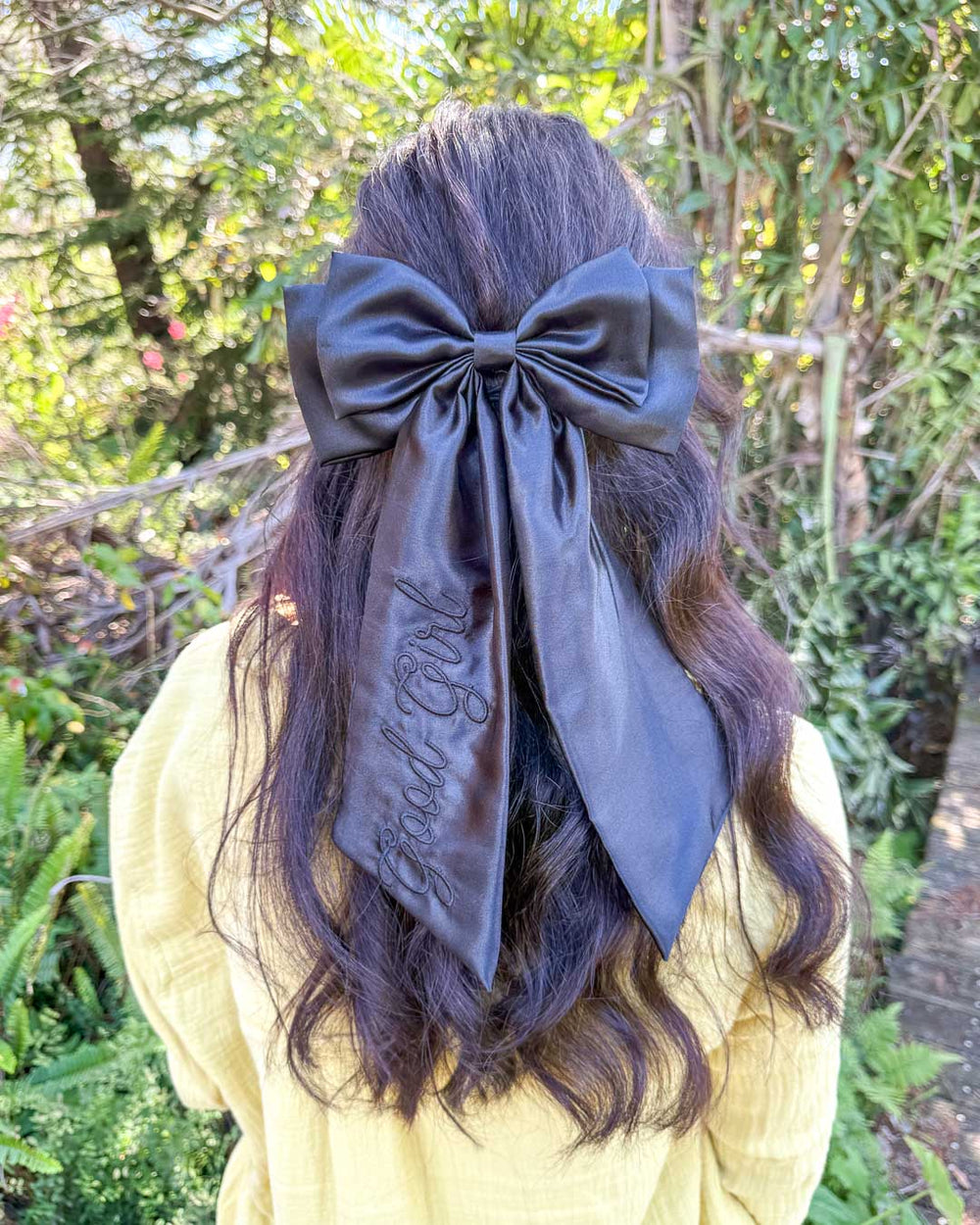Bookish hair accessory with shiny, black satin and the phrase 'Good Girl' embroidered on the hair bow.