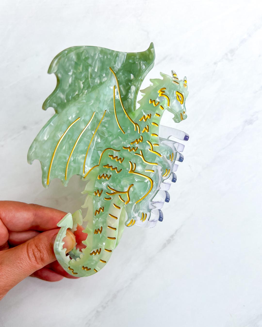 Fantasy reader hair clip with green and gold detailing in the shape of a dragon with its wings spread.