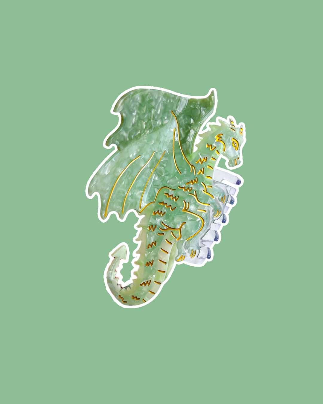 A fantasy hair claw clip with green tones and gold etching details in the shape of a dragon.
