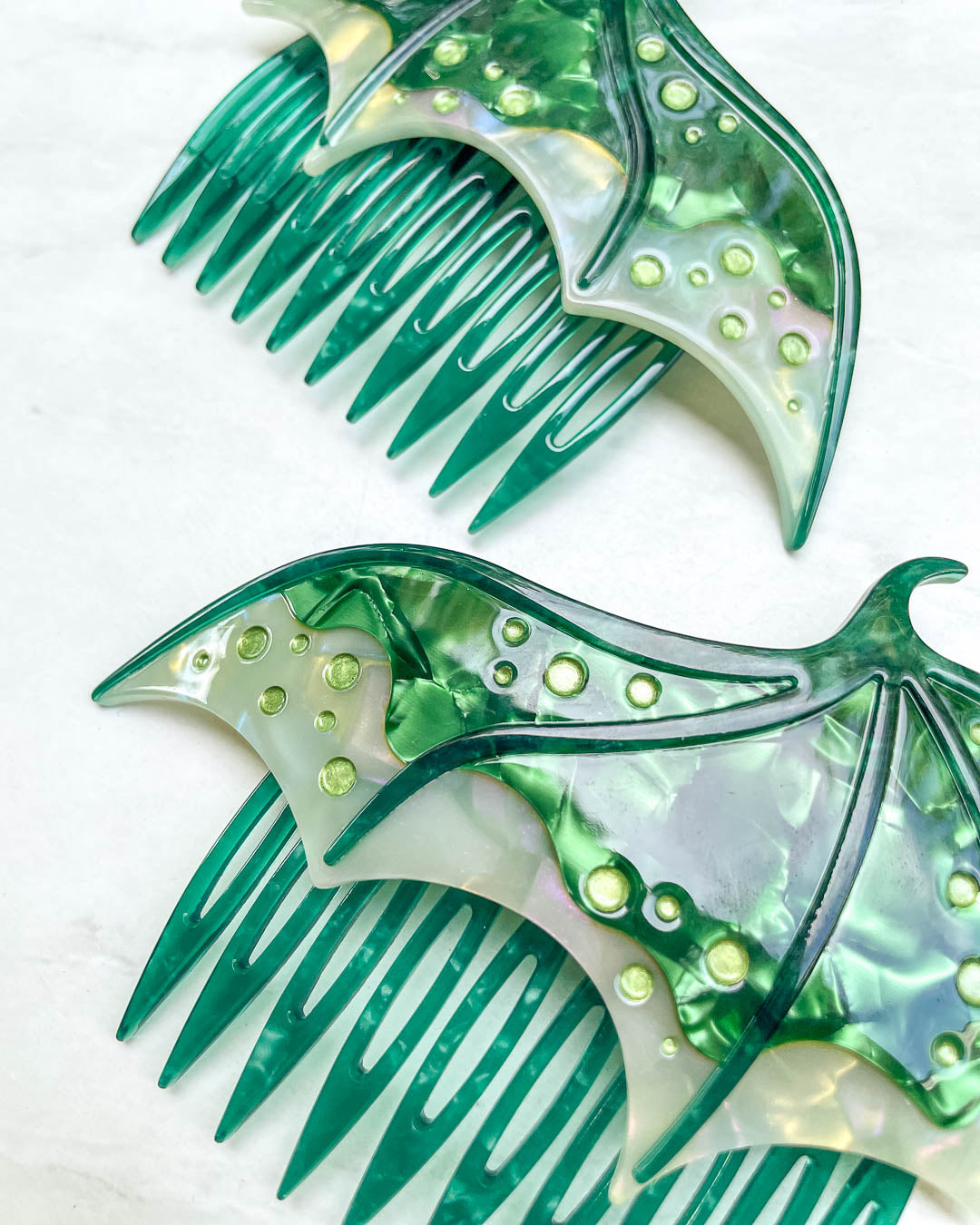 Close up of a fantasy hair accessory in the shape of dragon wings, featuring two combs in a green pearlescent color and engraved details.