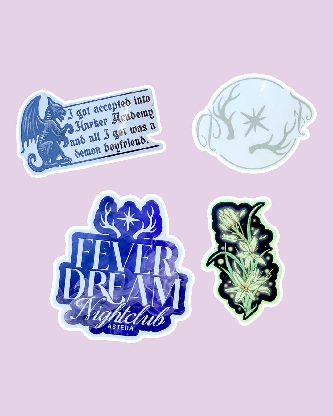 Three stickers and a tattoo inspired by Kate Golden's Half City on a pink background, featuring one with a gargoyle and the phrase "I got accepted into Harker Academy and all I got was a demon boyfriend," a temporary tattoo with antlers bracketing a star with 'F' and 'D' written in script as an indication of the club "Fever Dream" from the fantasy book, a Fever Dream Nightclub sticker in blue with the antlers and star design, and a glowing asphodels sticker.