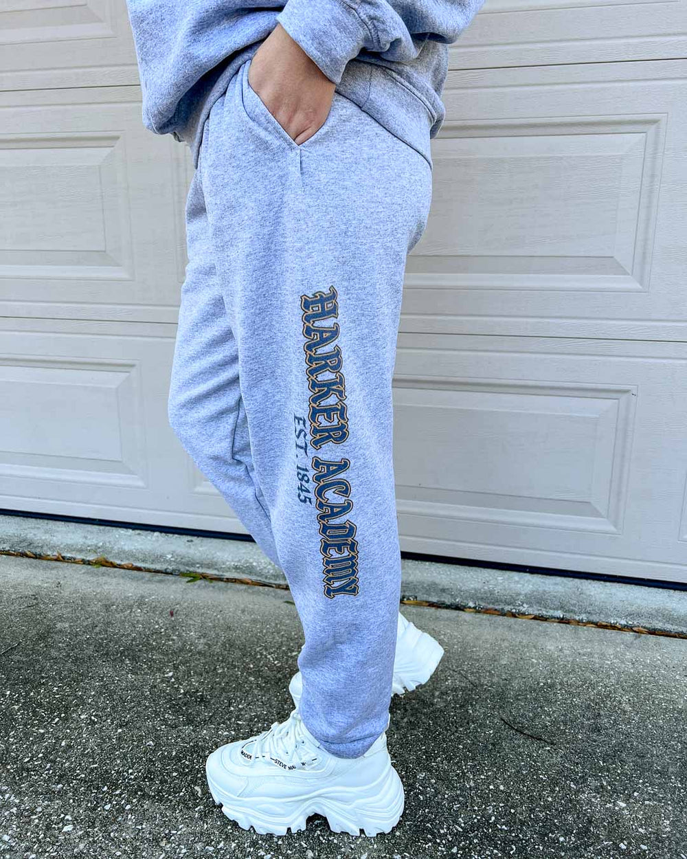 Model wearing gray sweatpants with "Harker Academy, EST. 1845" down the left pant leg, inspired by Kate Golden's fantasy book Half City.