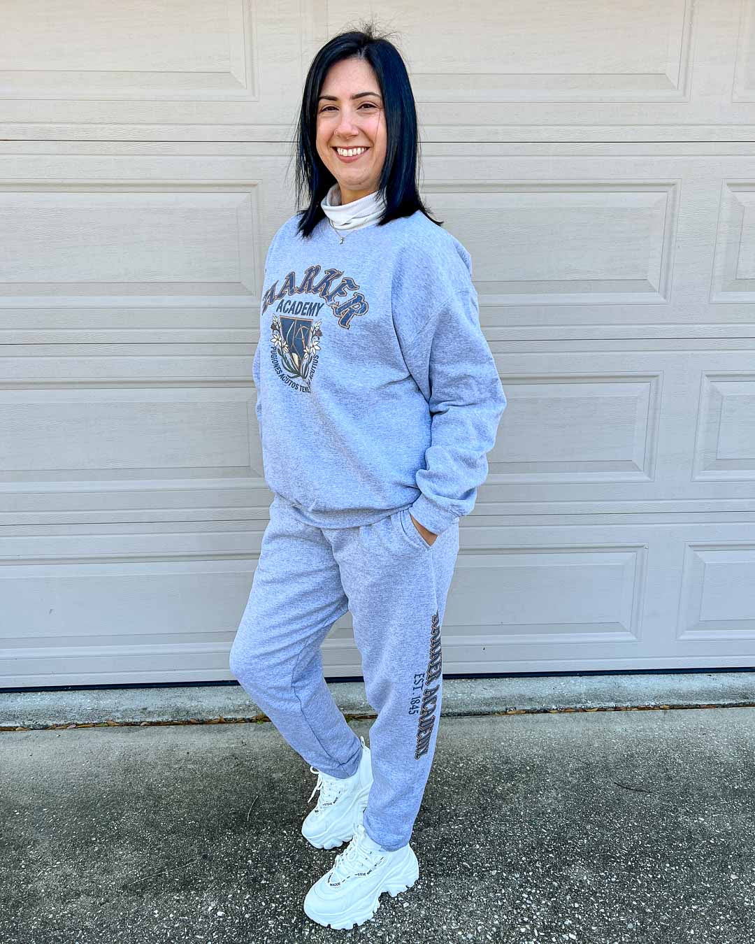 Woman wearing a gray Harker Academy sweatshirt and matching sweatpants with "Harker Academy, EST. 1845" down the left pant leg.