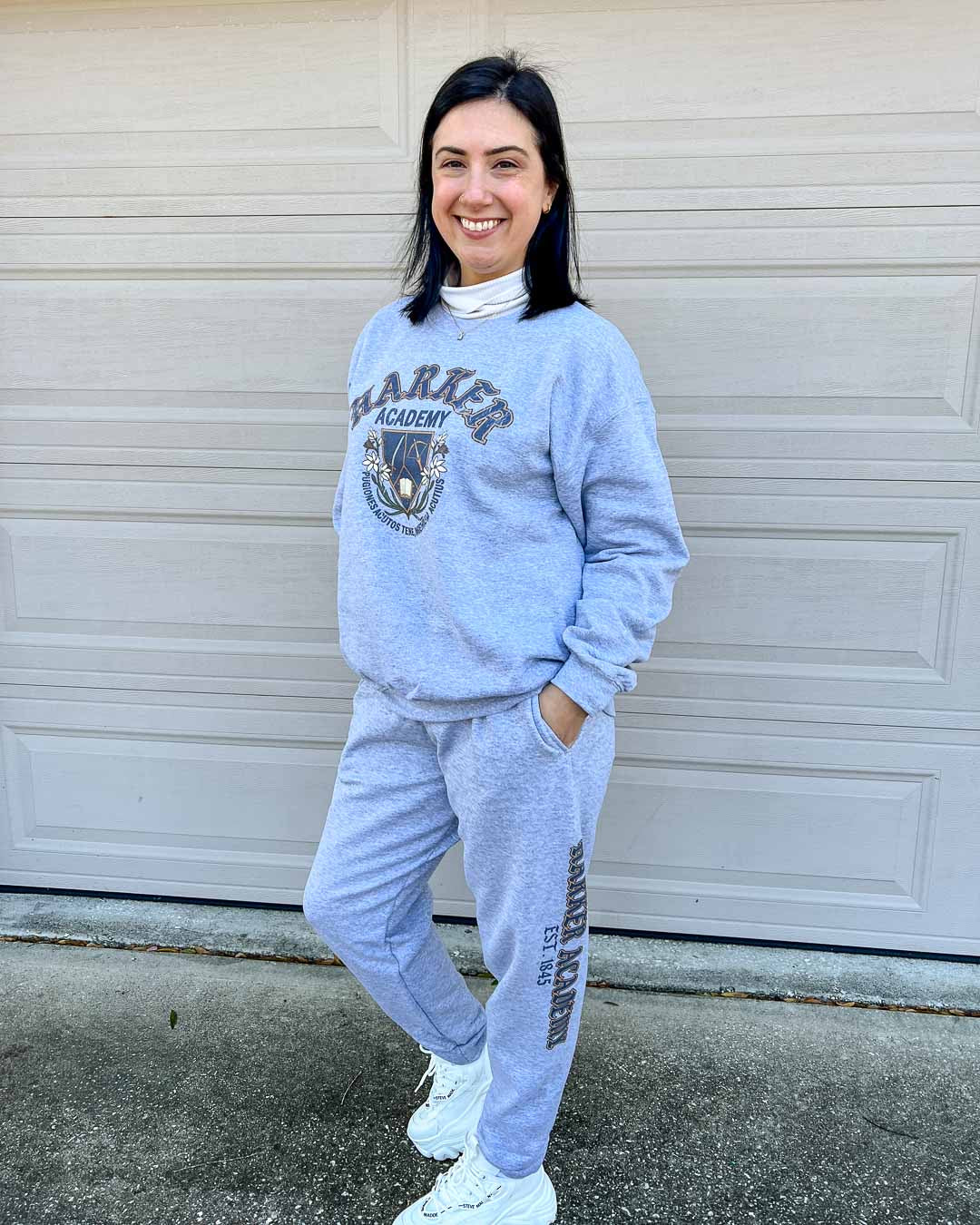 Woman wearing the matching Harker Academy sweatshirt and sweatpants set, featuring a Harker logo and motto on the sweatshirt, and "Harker Academy, EST. 1845" on the left pant leg.