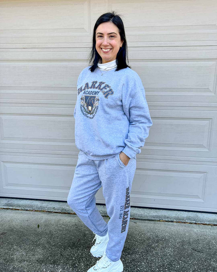 Woman wearing the matching Harker Academy sweatshirt and sweatpants set, featuring a Harker logo and motto on the sweatshirt, and "Harker Academy, EST. 1845" on the left pant leg.