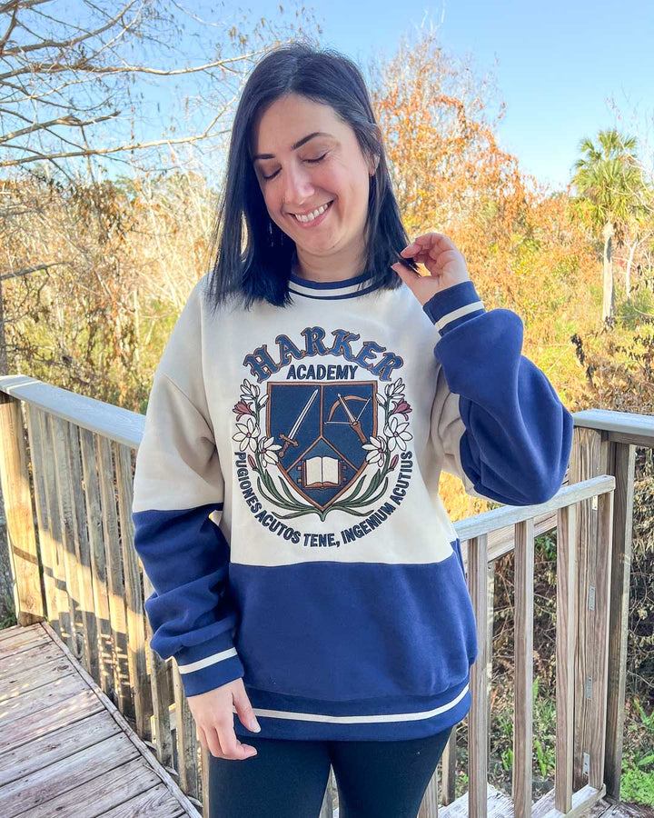 Model wearing blue and white Harker Academy sweatshirt with stripped details and a logo for the fictional magic school from Half City by Kate Golden.