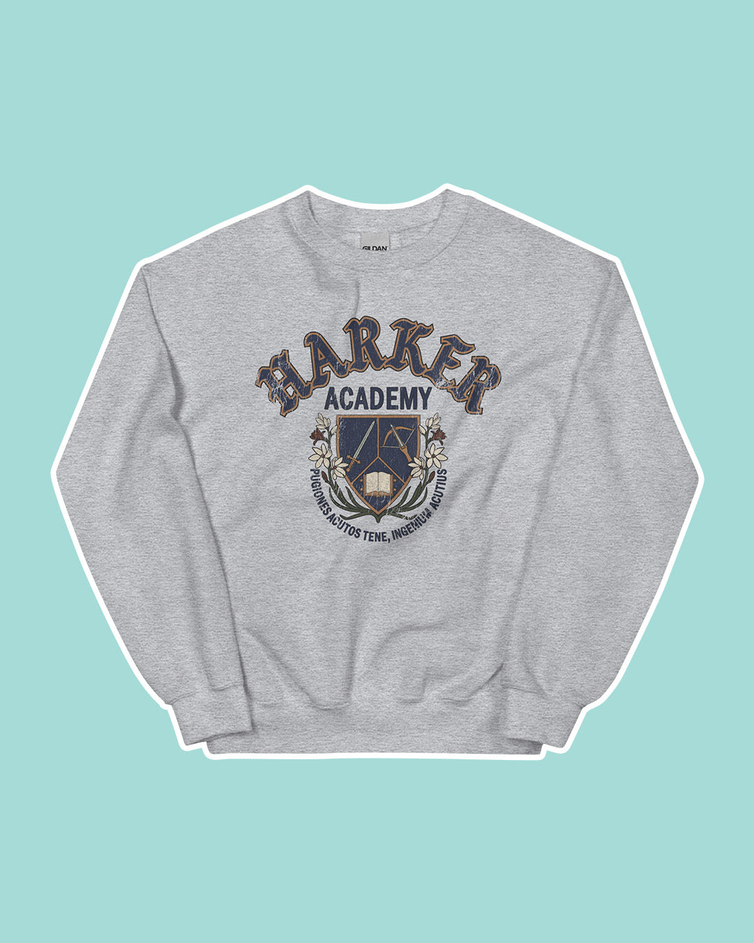 Gray crew neck sweatshirt on a light blue background featuring a Harker Academy logo for Kate Golden's Half City, including a shield with a sword, crossbow, and open book, as well as the motto curling under it reading "pugiones acutos tene, ingenium acutius."