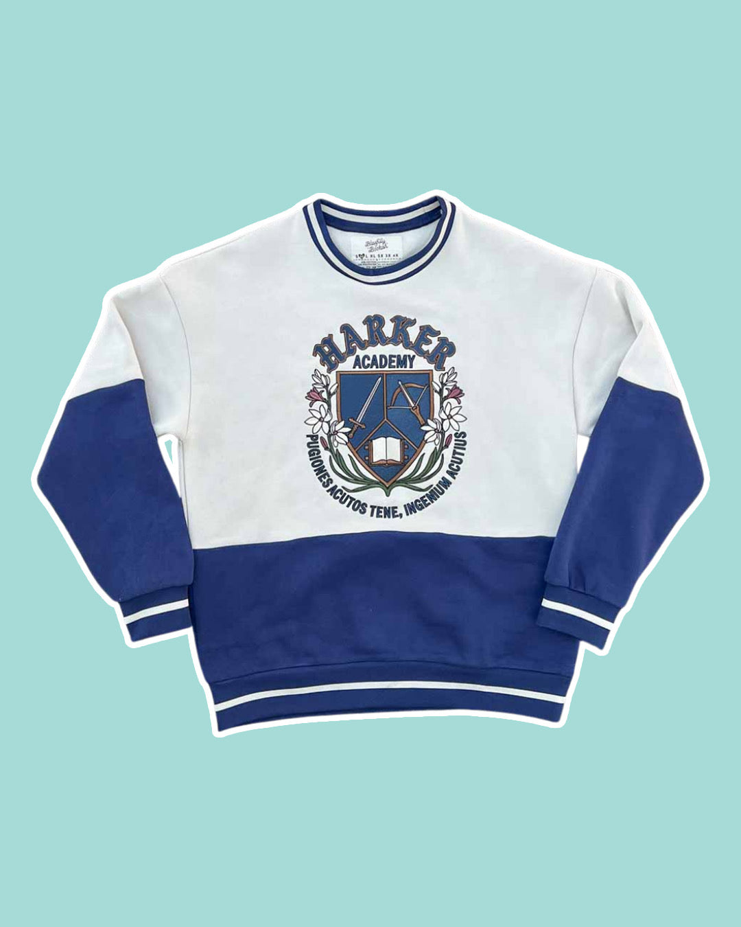Dual-tone crew neck sweatshirt on a light blue background featuring a Harker Academy logo for Kate Golden's Half City, including a shield with a sword, crossbow, and open book, as well as the motto curling under it reading "pugiones acutos tene, ingenium acutius."