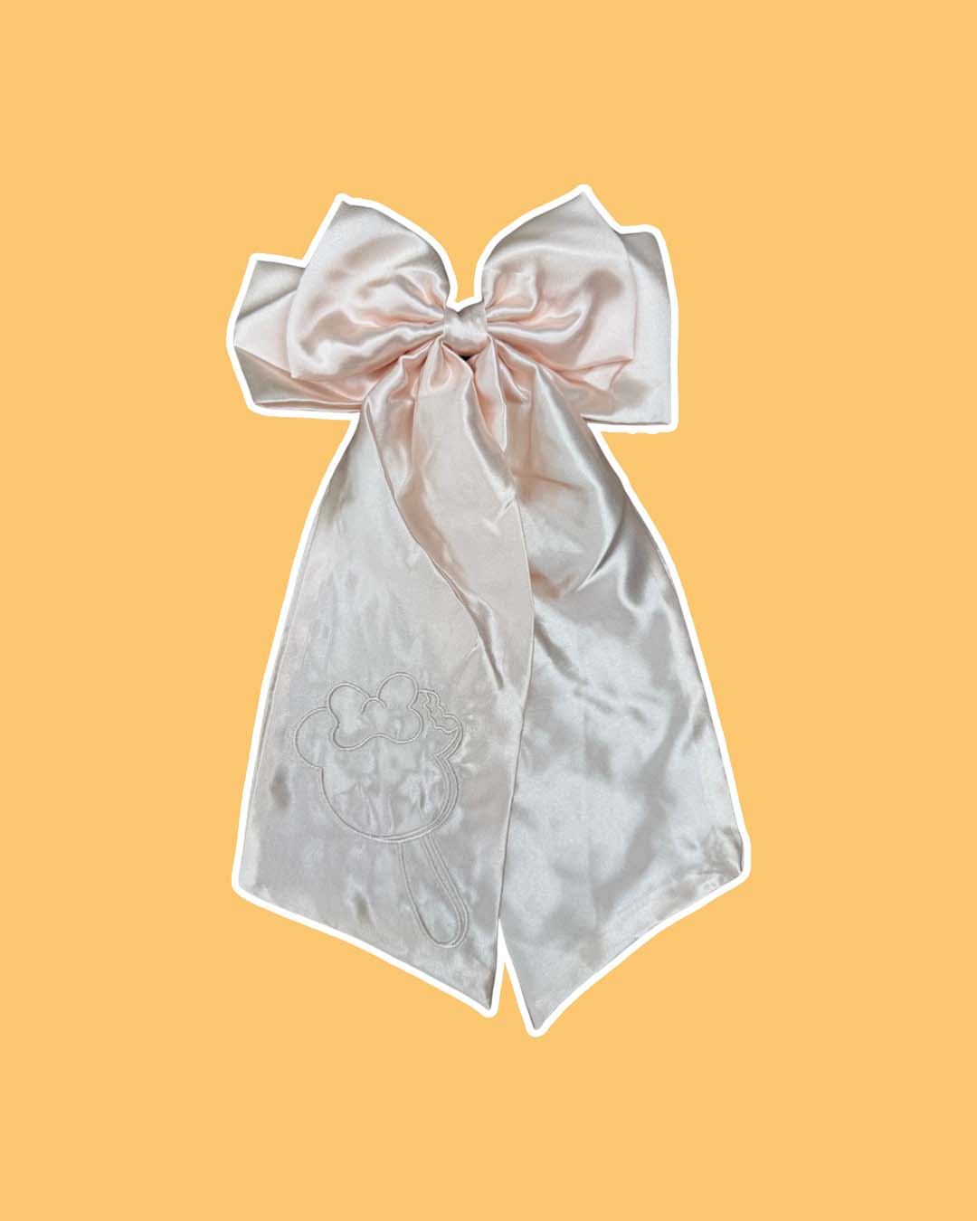 Cream satin hair bow clip featuring an embroidered mouse ear ice cream bar with a bow and a bite out of the right ear on a yellow background.
