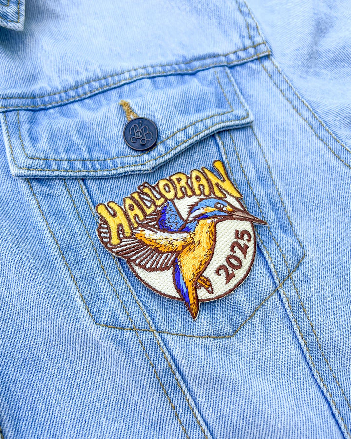 Blue denim jacket with the Halloran patch on it featuring a kingfisher with &