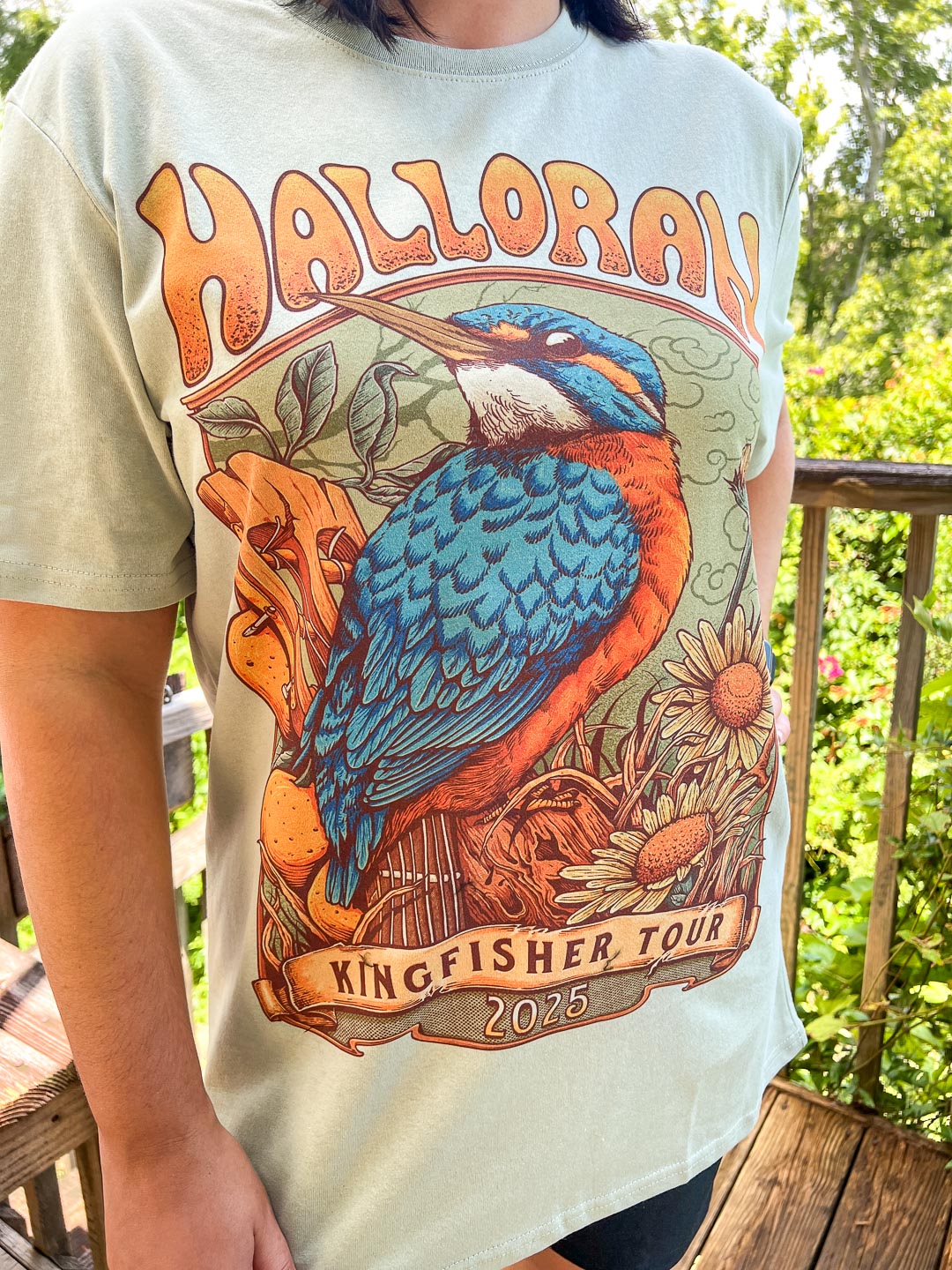 Light green Kate Golden t-shirt featuring a kingfisher perched on a guitar surrounded by wildlife with the text &