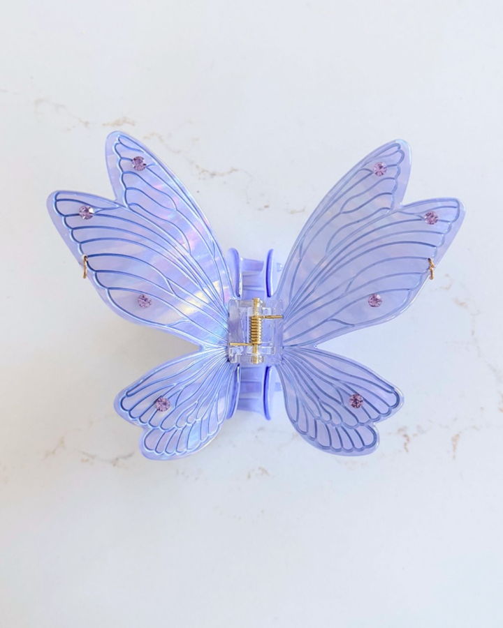 Lavender fairy wing hair clip for fantasy lovers featuring an iridescent shine to the wings and jewel embellishments against a white marble background.