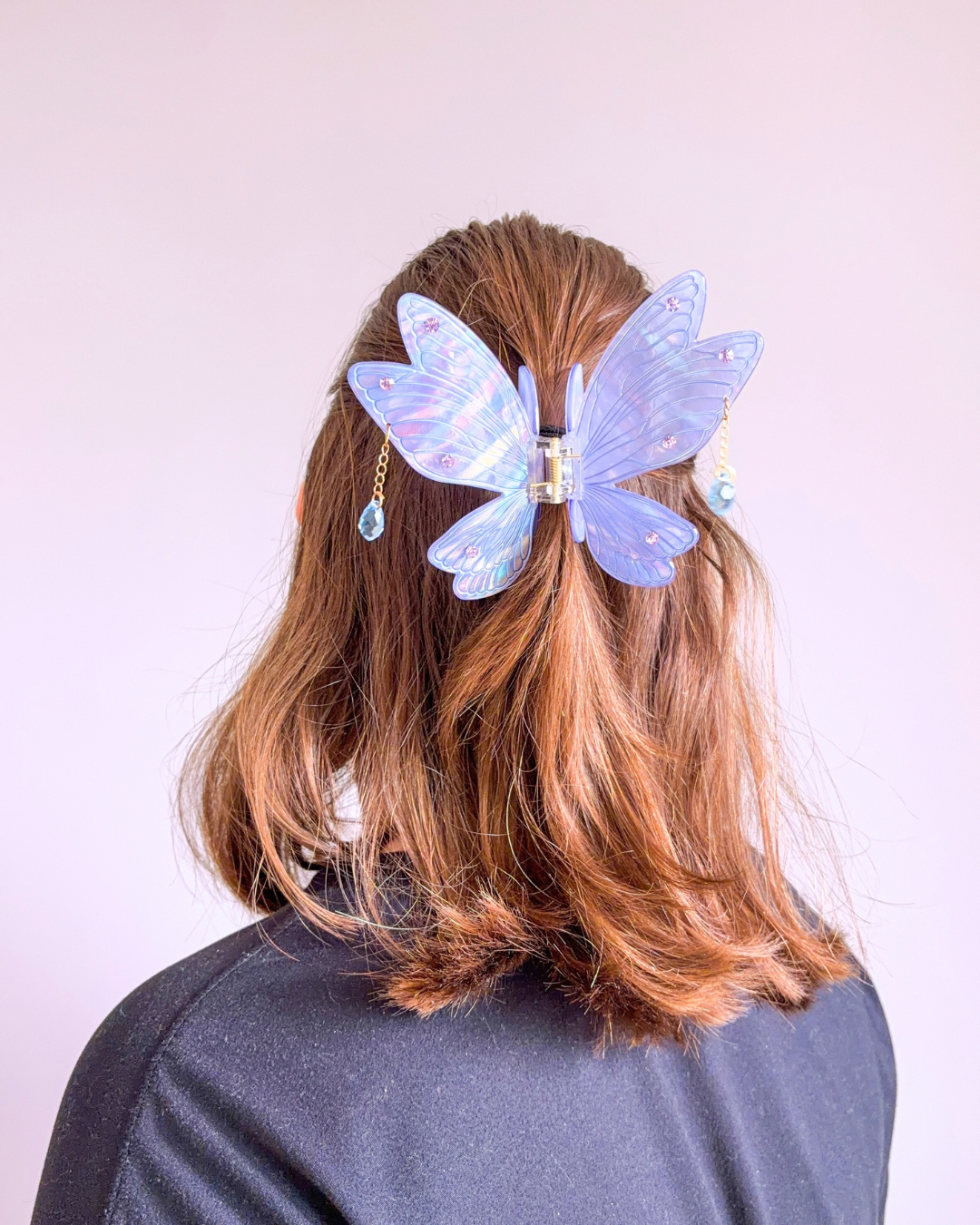 Woman with short brown hair wearing an iridescent purple fairy wing hair clip for fantasy readers with dangling gems off the sides and etching and gem embellishments, against a light purple background.