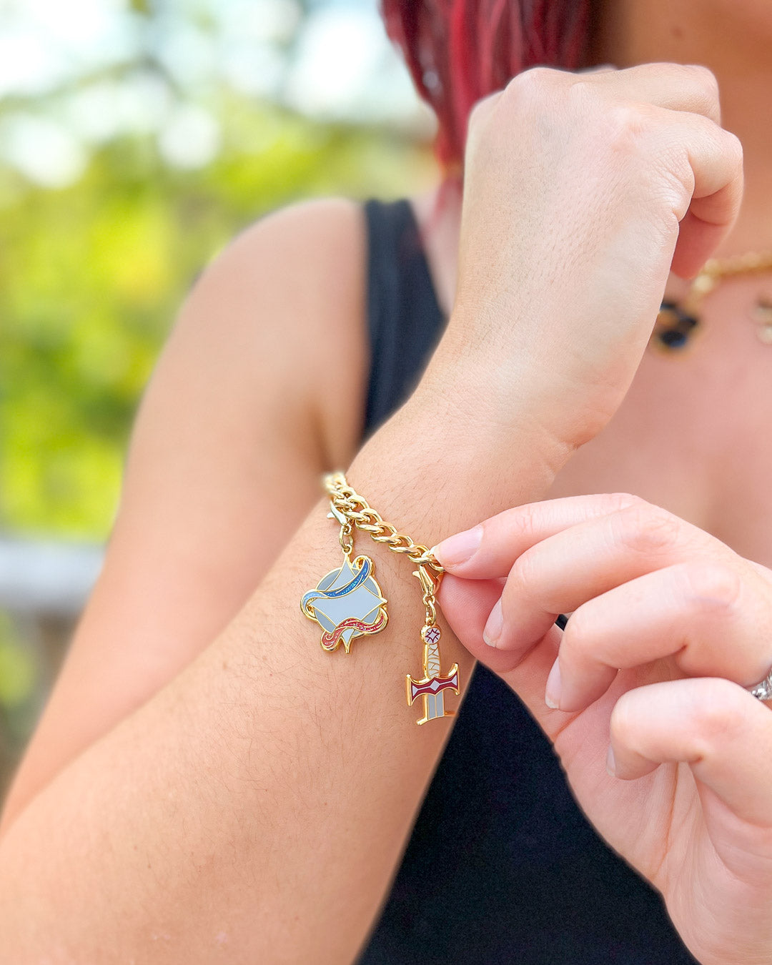Legendborn charms modeled on a wrist featuring the Legendborn symbol and Excalibur.