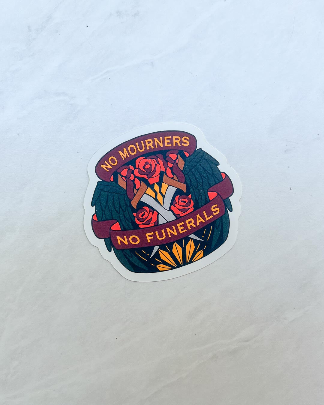 No Mourners No Funerals sticker for Six of Crows fans featuring an illustrated design of swings, roses, and crossed swords.