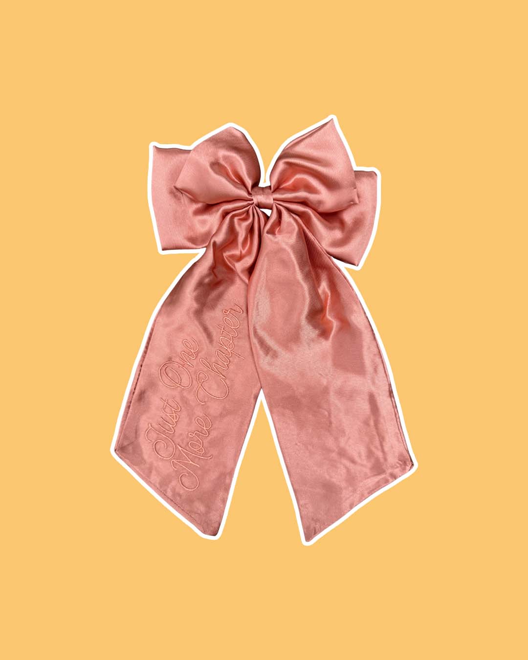 Pink satin hair bow embroidered with 'Just One More Chapter' in script text on the left tail.