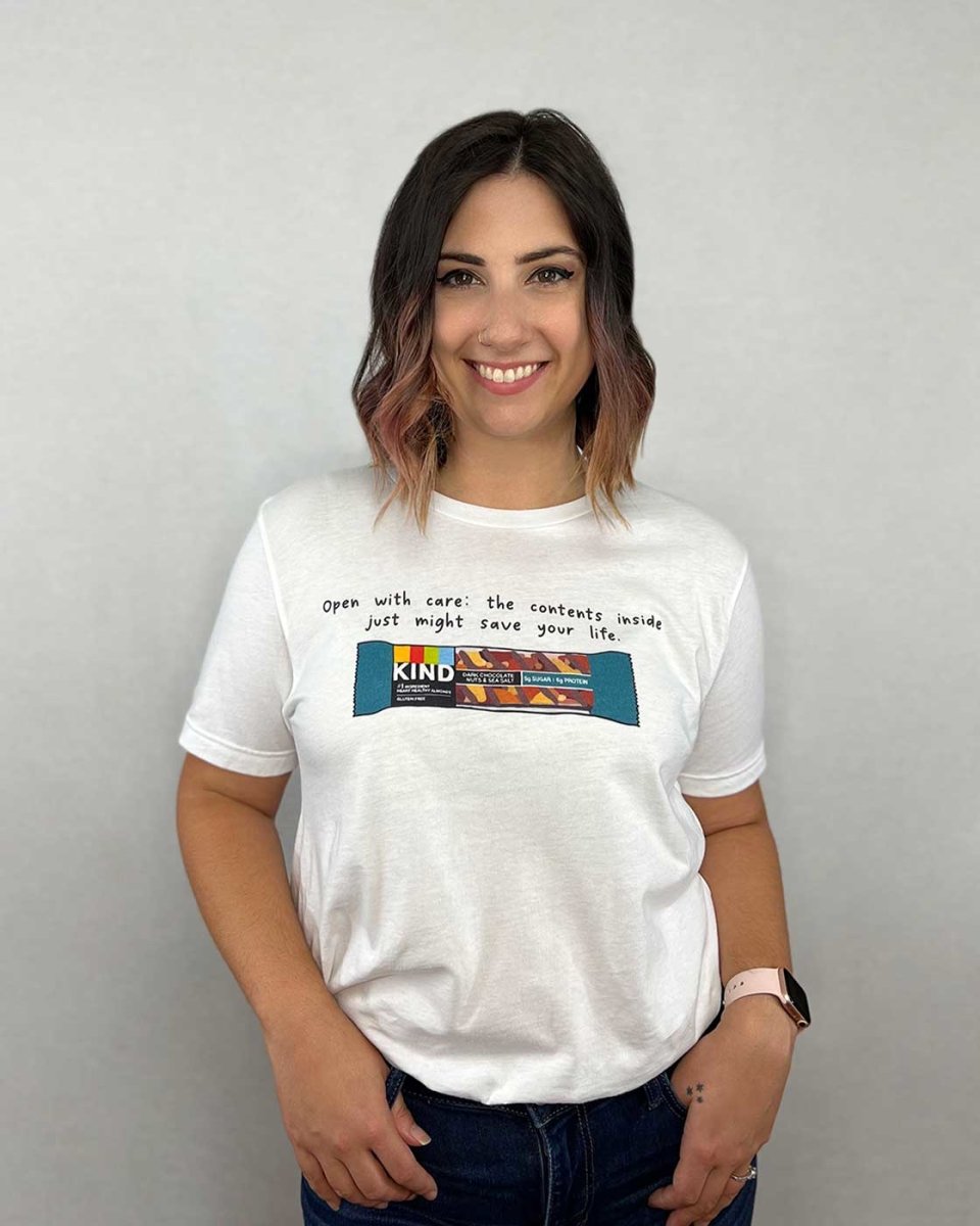 Wild is the Witch shirt for Rachel Griffin fans featuring the quote 'Open with care: the contents inside just might save your life' over Pike's favorite snack: a Kind bar.