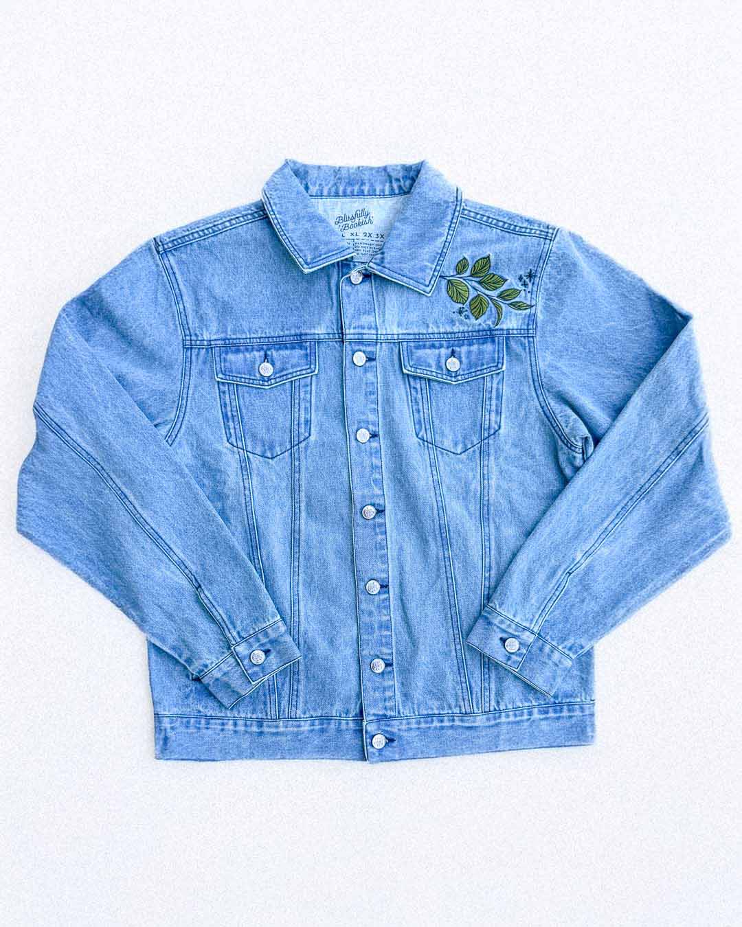Front of an embroidered fantasy jacket for mythology fans featuring light wash denim and an embroidered shoulder design of leaves.