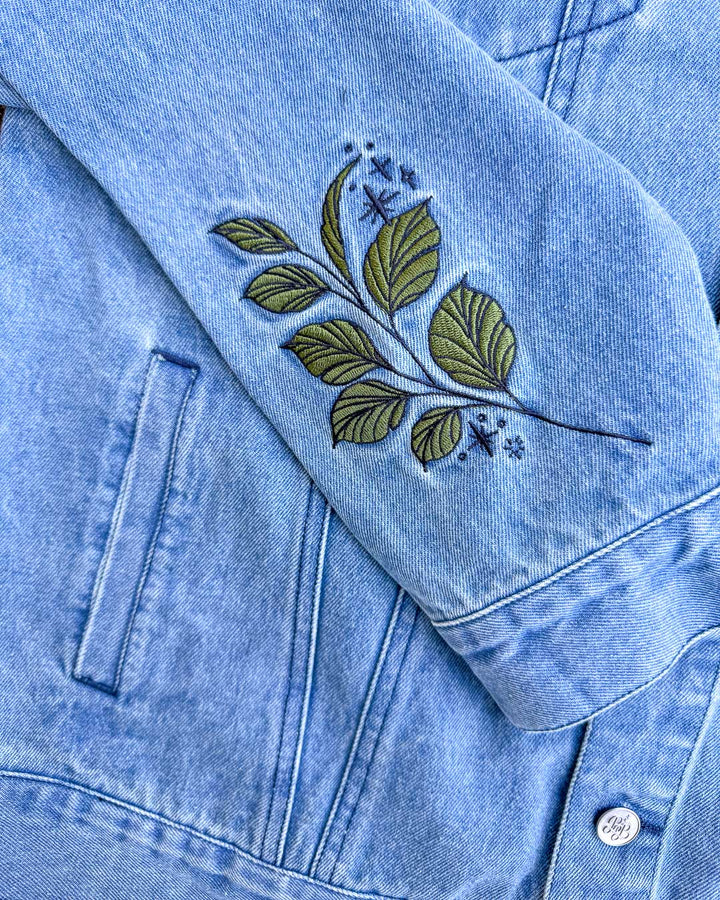 Close up of the sleeve design for the Persephone denim jacket, featuring embroidered leaves and stars.