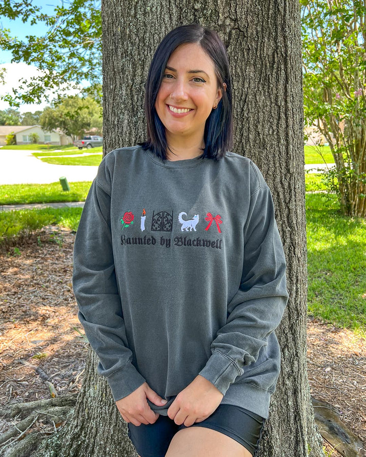 Kaylie Smith sweatshirt featuring five embroidered designs of a rose, a candle, gates, a white cat, and a bow with &