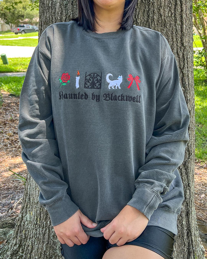 Woman modeling the embroidered Phantasma sweatshirt featuring embroidered designs of a rose, candle, gates, white cat, and bow over the phrase &