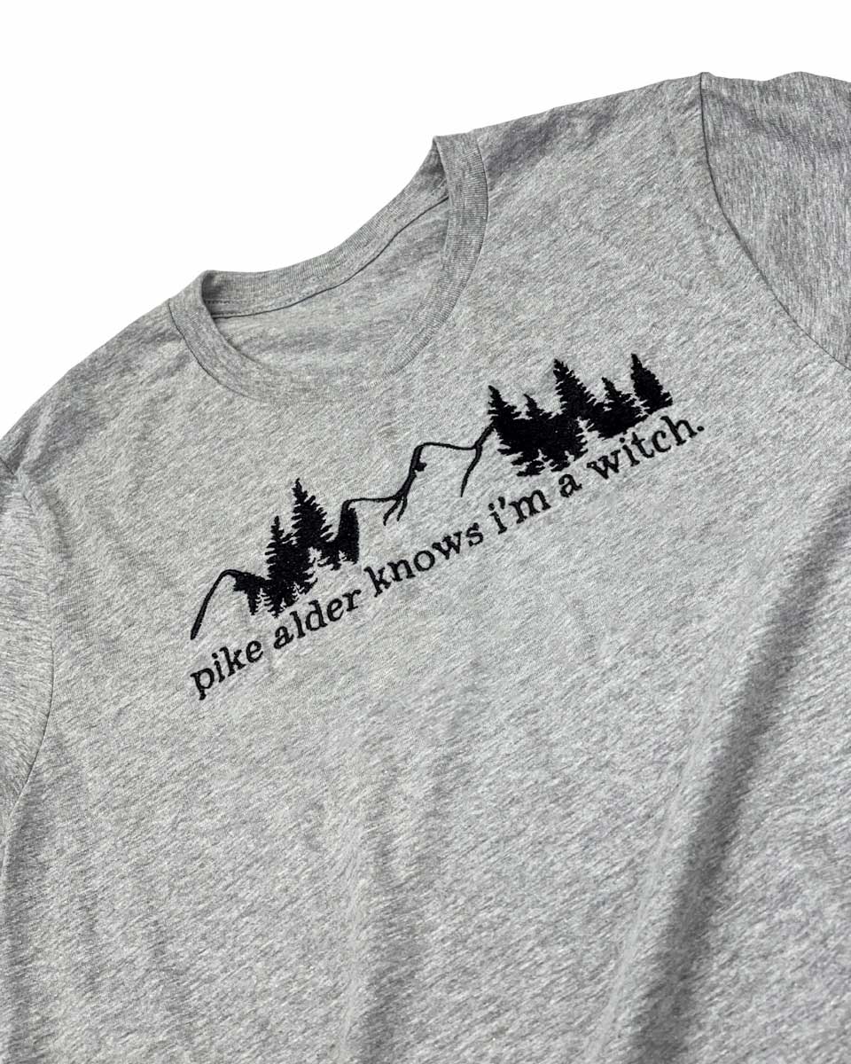 Embroidered shirt for Wild is the Witch fans featuring a black-thread outline of mountains and pine trees and the quote &