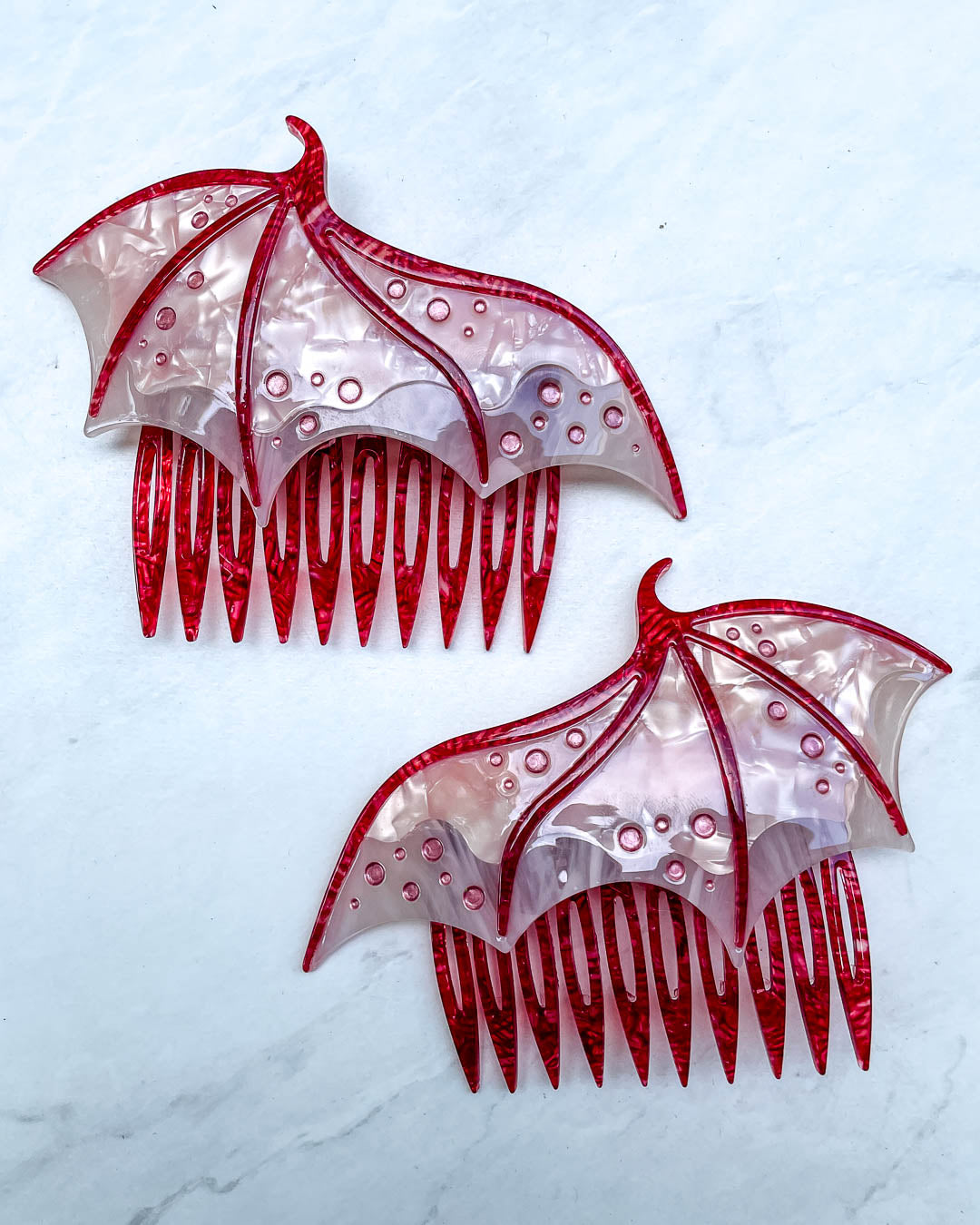 Hair combs for fantasy fans featuring two pink combs in the shape of dragon wings with engraved embellishments and a pearlescent pink color.
