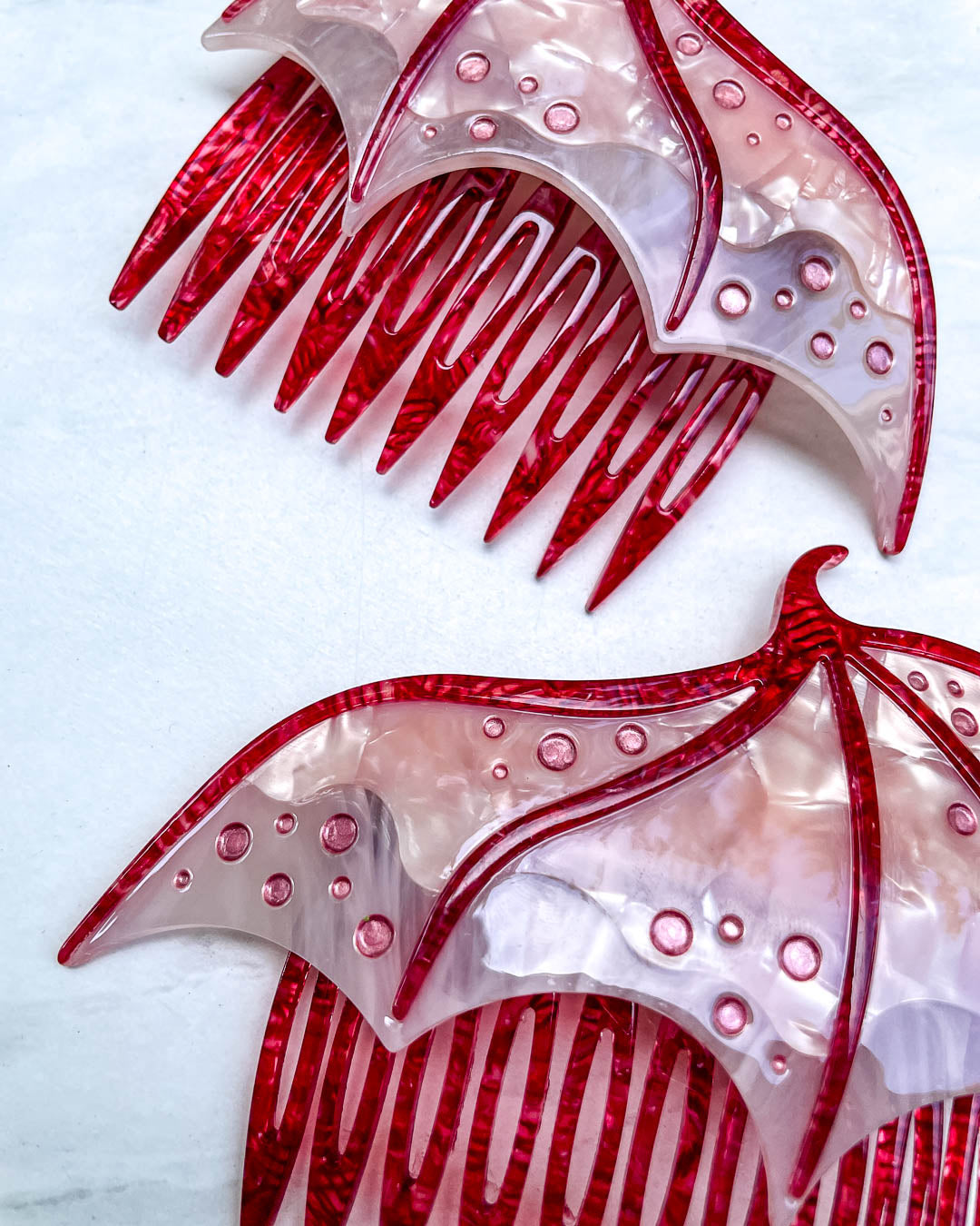 Close up of a fantasy hair accessory in the shape of dragon wings, featuring two combs in a pink pearlescent color and engraved details.