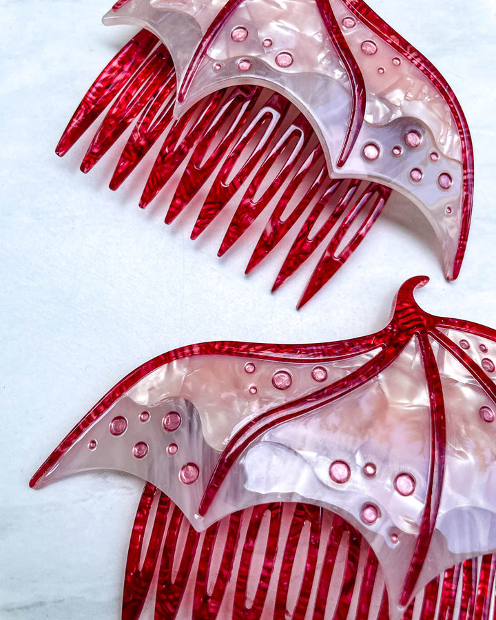 Close up of a fantasy hair accessory in the shape of dragon wings, featuring two combs in a pink pearlescent color and engraved details.