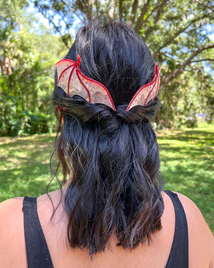 Fantasy hair combs featuring large combs in the shape of dragon wings in pink with engraved embellishments and a pearlescent color.
