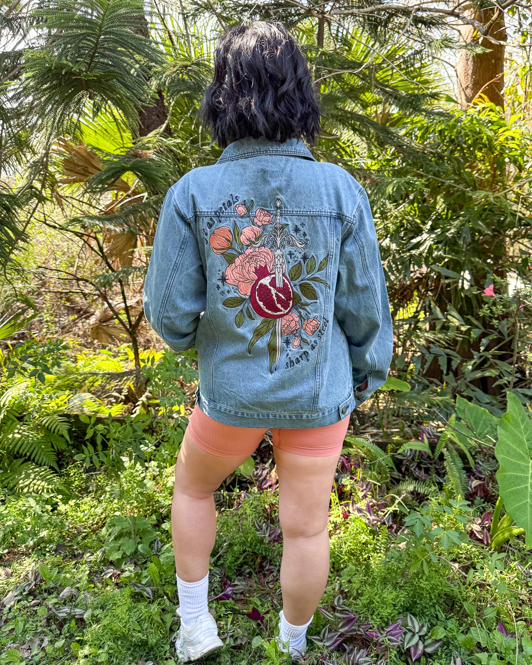 Embroidered Persephone outerwear featuring a large embroidered design on the back with a pomegranate, a silver sword, green leaves, pink roses, and the quote &