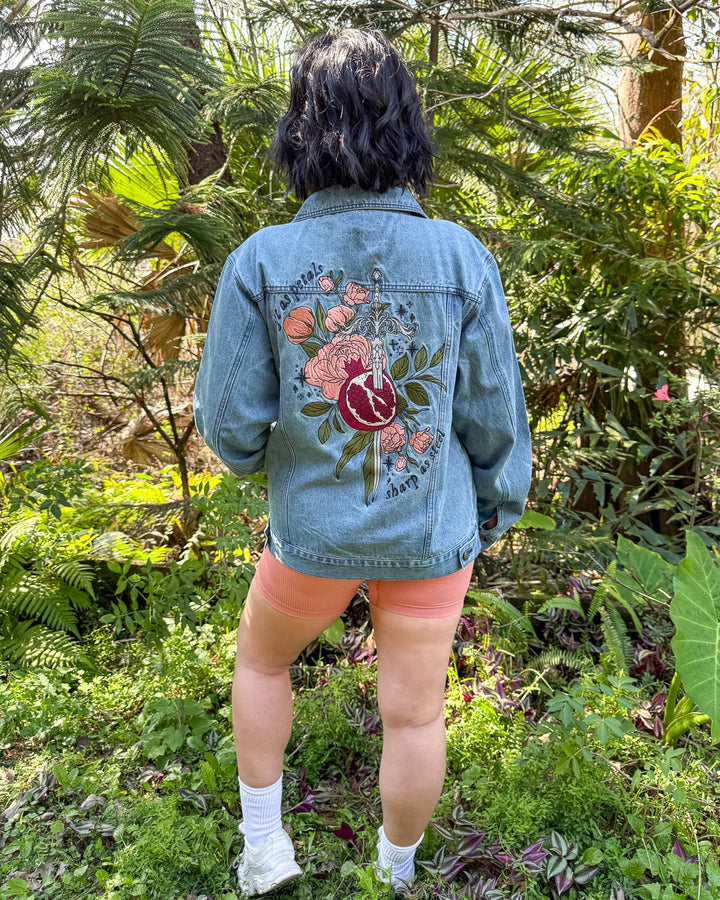 Embroidered Persephone outerwear featuring a large embroidered design on the back with a pomegranate, a silver sword, green leaves, pink roses, and the quote &