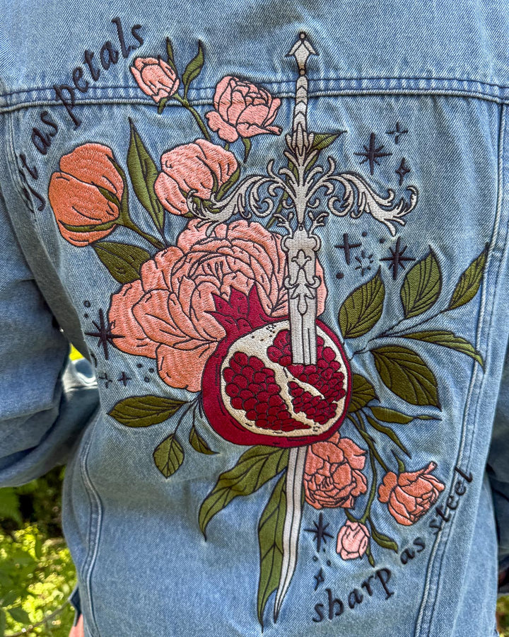 Embroidered outerwear for fantasy fans with an illustrated design of roses, stars, leaves, a sword, a pomegranate, and the quote &