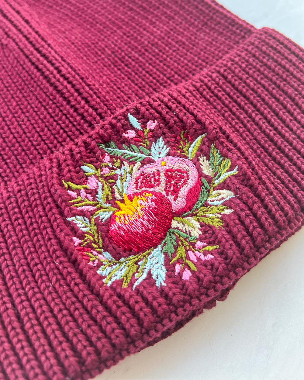 Close up of the red pomegranate beanie featuring the embroidered pomegranate, greenery, and flowers.