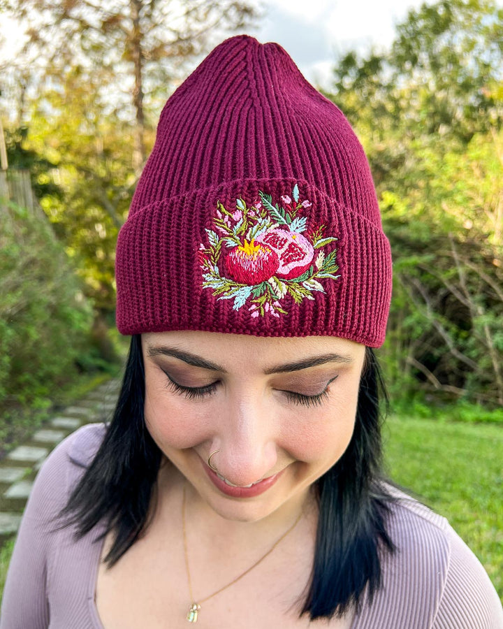 Rib knit beanie for fantasy readers featuring a pomegranate surrounded by embroidered flowers and greenery.
