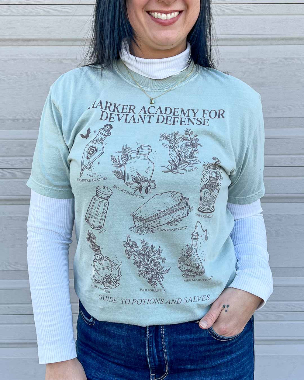 Woman wearing the Potions and Salves t-shirt featuring potion bottles and bits of weeds and flowers all illustrated in line art.