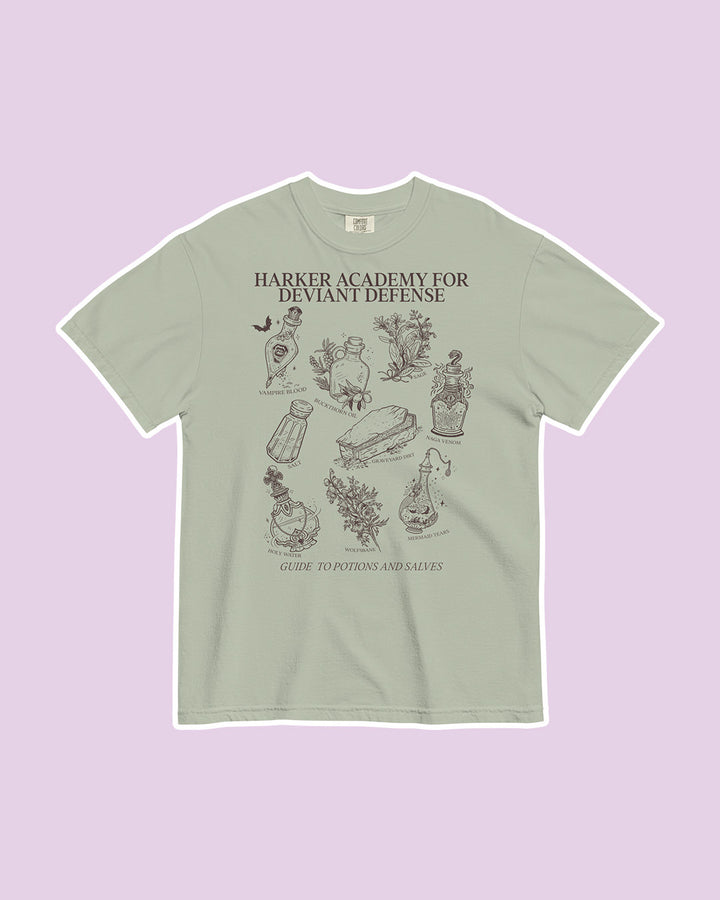 Light green t-shirt on a purple background featuring the text "Harker Academy for Deviant Defense" at the top with a number of line illustrated potion bottles and flora below it, labelled as a "Guide to Potions and Salves."