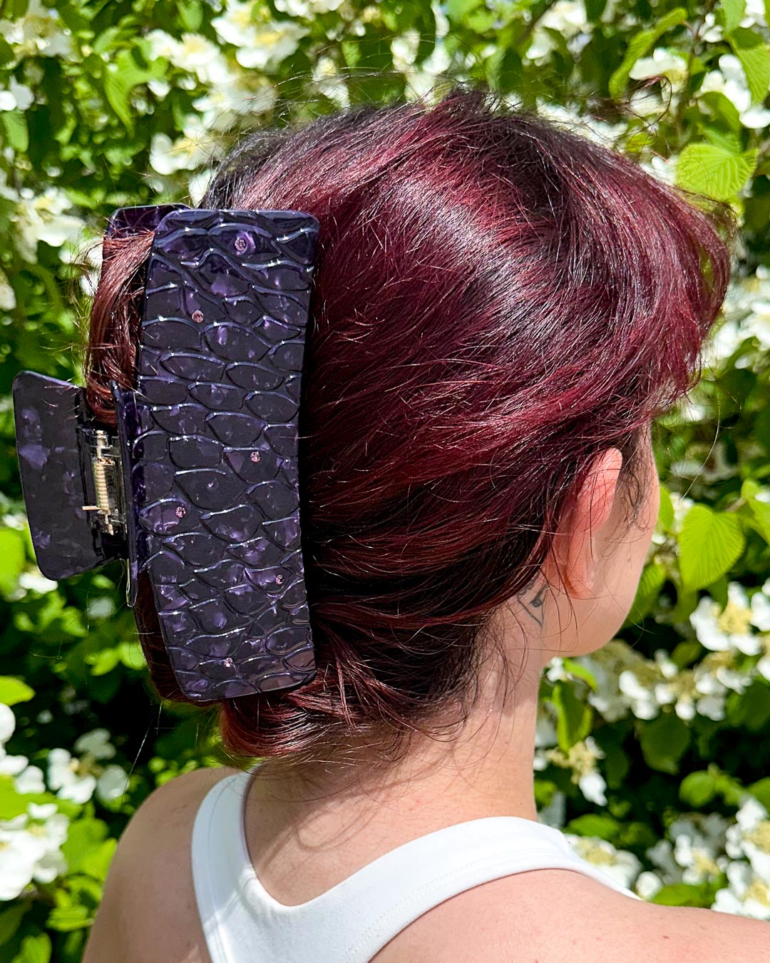 Hair clipped half-up-half-down with a purple pearlescent detailed bookish hair clip for fantasy readers designed to look like dragon scales with gem embellishments.